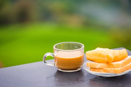 Coffee and deep-fried dough stick on wood table at the tea plantation in morning time.Thailandの写真素材
