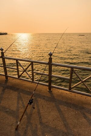 Fishing rod standing-up on the cement bridge by the sea during the sunsetの写真素材