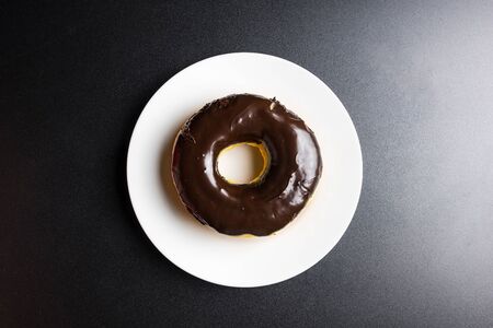 Chocolate frosted doughnut on a white plate on the black background Space for textの写真素材