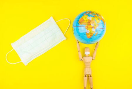Wooden figure mannequin carrying planet earth globe over head on a yellow background.の写真素材