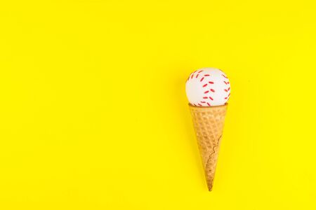 Baseball ball toy in ice cream waffle cone on yellow background in minimal style. Concept sports entertainment. Top view Copy space Template for text or your design.の写真素材