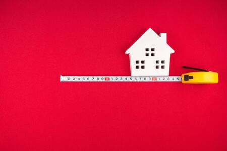 Wooden white house and measuring tape on red background with copy space.Real estate concept, New house concept, Finance loan business concept, Repair maintenance concept.の写真素材