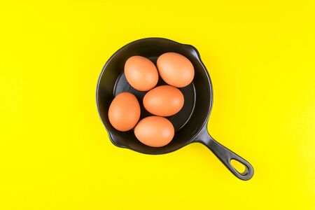 Top view of raw chicken eggs in frying pan on yellow background.の写真素材