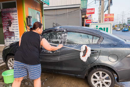 Bangkok, Thailand - April, 19, 2020 : Unidentified name Asian woman is washing a Mazda 2 car with a car wash shampoo. In front of the house in the evening at Bangkok, Thailandのeditorial素材