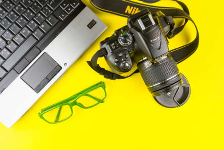 Bangkok, Thailand - March, 31, 2020 : Green frame glasses, Notebook computer and Dslr nikon d5300 isolated on yellow background.のeditorial素材