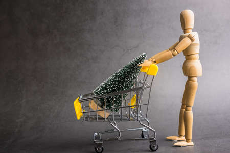 A wooden doll carries a Christmas treel in metal shopping cart. Concept of buying Christmas...
