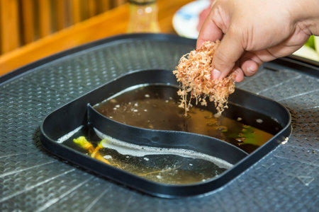 A woman's hand is putting dried oysters in broth in an electric stove to make Japanese broth.の写真素材
