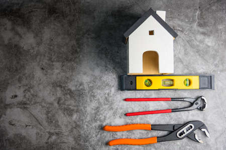 Wooden white house toy and construction tools on Gray-black cement floor background with copy space.Real estate concept, New house.Home repair conceptの写真素材