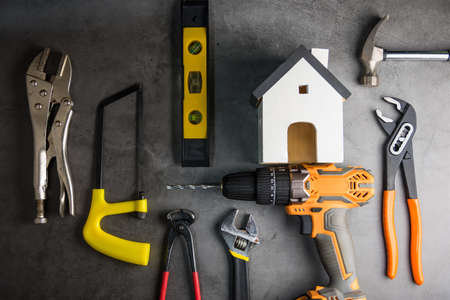 Wooden white house toy and construction tools on Gray-black cement floor background with copy space.Real estate concept, New house.Home repair conceptの写真素材