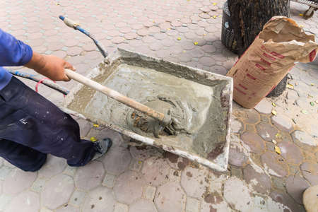 Bangkok, Thailand - February, 17, 2021 : Worker shovels a wet mix of concrete from a wheelbarrow at curb block installation at Bangkok, Thailandのeditorial素材