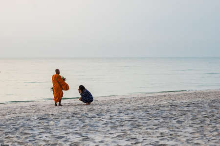 Prachuap Khiri Khan, Thailand- April, 04, 2021 : Sunrise with reflection on the sea and beach that have blurred silhouette photo of buddhist monk walking alms offering food in the morning on beach of Thailand.のeditorial素材