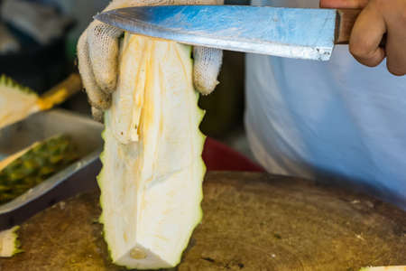 Peel durian fruit with a knife, an Asian woman's hand Durian is the king of fruits. Released only in...