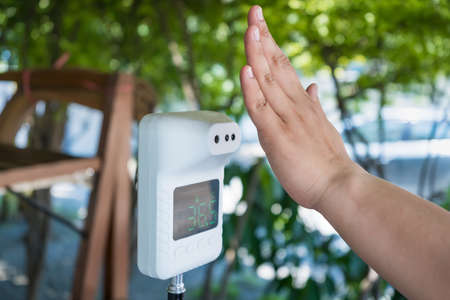 Asian woman checking forehead temperature using infrared thermometer before enter establishment with focus on thermometer.の写真素材