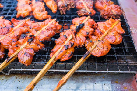 Grilled chicken with wooden stick on charcoal grill at street market in Bangkok, Thailand. Chicken is the main subjectの写真素材