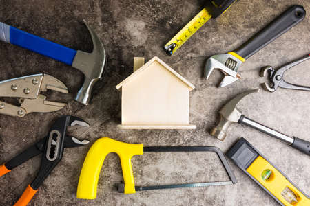 Wooden white house toy and construction tools on Gray-black cement floor background with copy space.Real estate concept, New house.Home repair conceptの写真素材