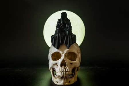 A statue of a grim reaper sitting on a skull on a full moon background.の写真素材