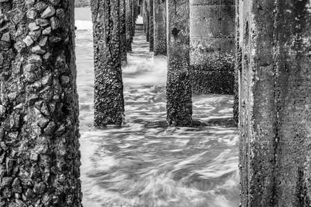 Black and white image of View Under the bridge walkway at the pier from the beach to the...