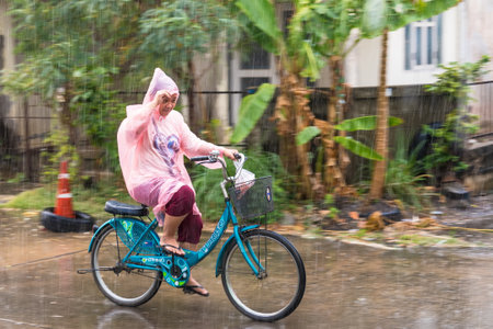 Bangkok, Thailand - February, 14, 2023 : A woman in a raincoat is riding her bike in the rain going home at Bangkok, Thailand.のeditorial素材