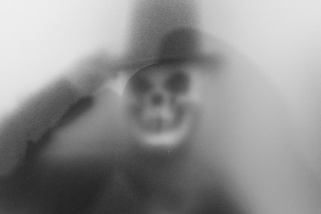 Bangkok, Thailand - August, 20, 2023 : Shadow blur of horror man in ghost skull mask.Dangerous man behind the frosted glass.Mystery man.Blur picture.Add effects noise and grain.Concept Halloween.の写真素材