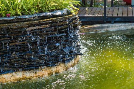 A serene garden with water flowing from a fountain into a pond surrounded by nature and treesの写真素材