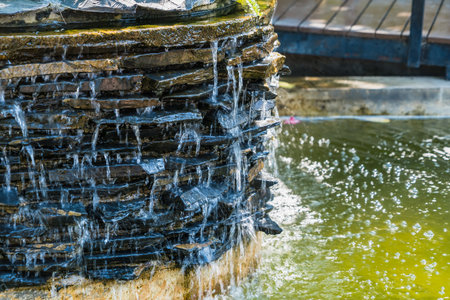 A serene garden with water flowing from a fountain into a pond surrounded by nature and treesの写真素材