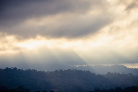 A breathtaking view of sun rays piercing through thick clouds, illuminating the misty mountain range below.の写真素材