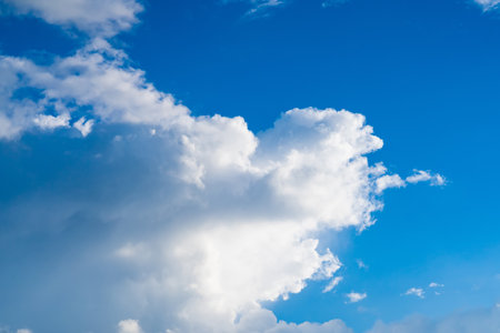 The sunlight illuminates the clouds, giving them a soft, radiant appearance. The blue sky in the background is clear, with a gradient of lighter hues towards the horizon.の写真素材
