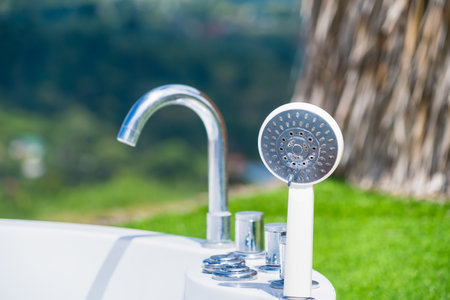 A modern bathtub featuring a handheld shower and faucet, with a scenic view.の写真素材