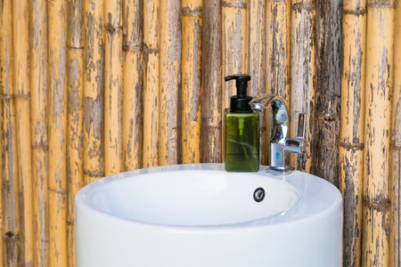 A bathroom sink with a green soap dispenser, chrome faucet, and bamboo wall, combining eco-friendly and modern elements.の写真素材