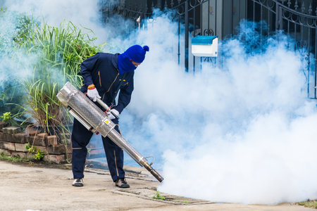 A health worker uses a fogging machine to control mosquito populations in an urban setting.のeditorial素材