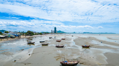 Traditional fishing boats stranded on a muddy shore during low tide, with a coastal villageの写真素材