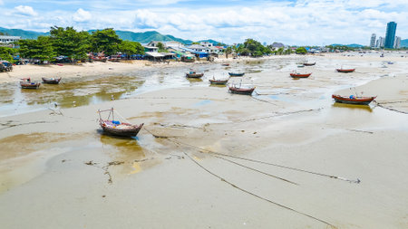 Traditional fishing boats stranded on a muddy shore during low tide, with a coastal village