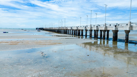 A tranquil pier extending into the sea during low tide, with reflections in the shallow water and a clear blue sky above.の写真素材