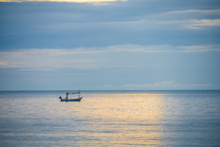 A fishing boat floats on calm waters in the early morning, creating a serene and peaceful scene.の写真素材