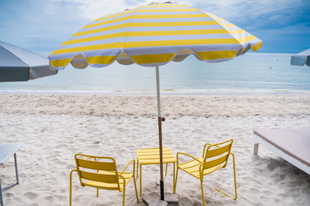 A vibrant yellow umbrella paired with two matching chairs on a sandy beach, creating a cheerful and inviting seaside setting.の写真素材
