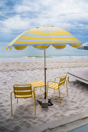 A vibrant yellow umbrella paired with two matching chairs on a sandy beach, creating a cheerful and inviting seaside setting.の写真素材