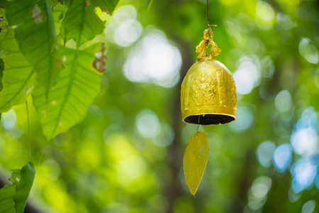 A golden bell hangs from a tree branch, its intricate design reflecting the sunlight. The sound of the bell ringing fills the air with a sense of peace and tranquility.の写真素材