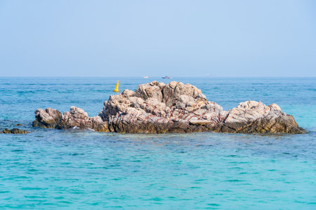 Discover a pristine paradise where a rocky islet is surrounded by the tranquil turquoise waters of the ocean.の写真素材