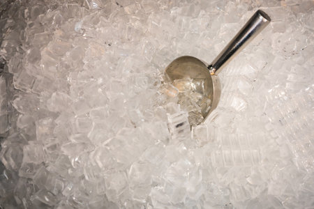 This image features crystal clear ice cubes piled high with a sleek stainless steel scoop. Perfect for showcasing refreshing beverages or adding a cool touch to your culinary creations.の写真素材