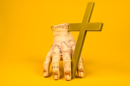 This image of a severed hand holding a cross against a bright yellow background invites viewers to...