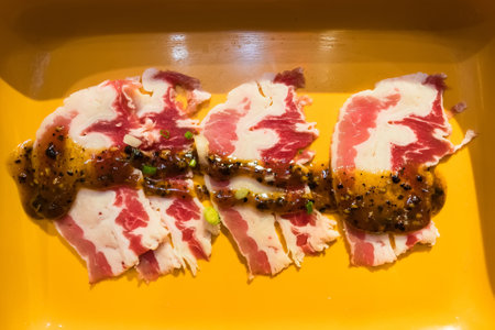 Fresh slices of marbled beef with black pepper sauce arranged on a yellow plate.の写真素材