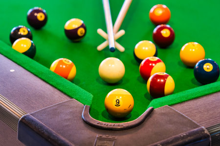 The image shows colorful numbered billiard balls arranged on a green felt pool table with a cue stick in the foreground, ready for a game. The close-up view highlights the vibrant setup and the anticipation of an engaging match.の写真素材