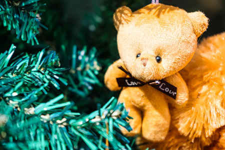 Soft brown teddy bear ornament hanging on a Christmas tree adorned with golden ribbon and vibrant red baubles, adding warmth and charm to festive holiday decor.の写真素材