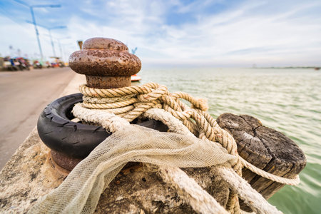 An old mooring post with rope and tire on a seaside pier, highlighting its detailed nautical features.の写真素材