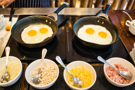 A professional kitchen scene with perfectly fried eggs garnished with assorted fresh toppings like mushrooms, tomatoes, and herbs, showcasing a gourmet breakfast preparation.の写真素材