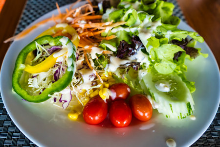 This vibrant garden salad features a mix of fresh vegetables, including lettuce, bell peppers, cherry tomatoes, and carrots, all topped with a creamy dressing.の写真素材