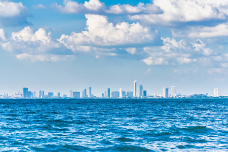 A vibrant cityscape view across the ocean with stunning blue waters and puffy clouds, creating a picturesque scene.の写真素材