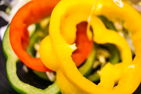 A close-up view of freshly sliced bell peppers in red, green, and yellow colors, highlighting their vibrant hues and fresh textureの写真素材