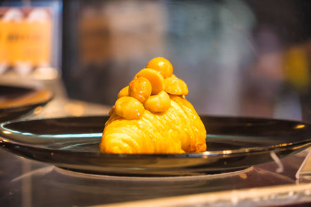 A golden croissant topped with glazed macadamia nuts, served on a black plate, perfect for breakfast...