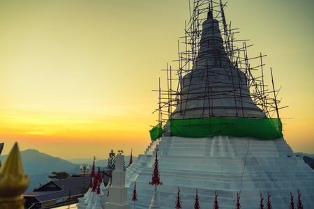 Phetchabun, Thailand - January, 06, 2025 : Golden Sunrise Over a Temple Under Construction with Mountain Backdrop at Phetchabun, Thailand.の写真素材